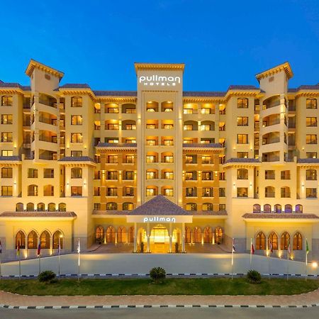Pullman Resort Al Marjan Island Ras al-Khaimah Exterior photo The photo shows a modern hotel building, likely part of the Pullman brand. The structure features a warm, inviting color scheme with multiple floors and architectural details such as balconies and large windows. It is illuminated, creating a welcomin