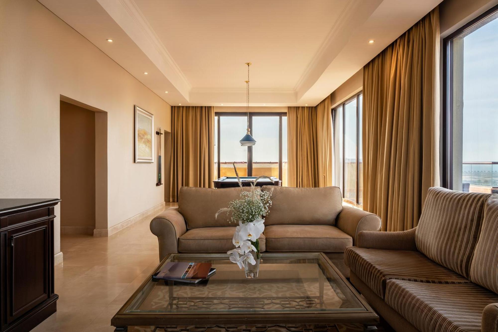 Pullman Resort Al Marjan Island Ras al-Khaimah Exterior photo The photo shows a stylish and modern living room. It features two comfortable sofas, one of which is a light beige color, and the other has a striped pattern. In the center, there is a glass coffee table adorned with a decorative vase containing whit