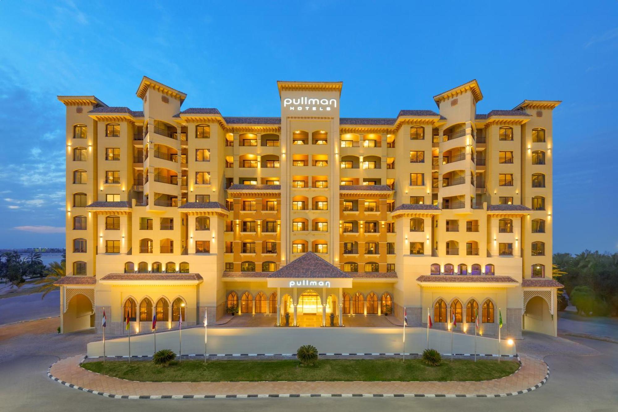 Pullman Resort Al Marjan Island Ras al-Khaimah Exterior photo The image shows a modern hotel building with multiple stories, likely indicating a luxury accommodation. It features a warm-toned exterior with a combination of traditional and contemporary architectural elements. The hotel's name, "Pullman," is prom
