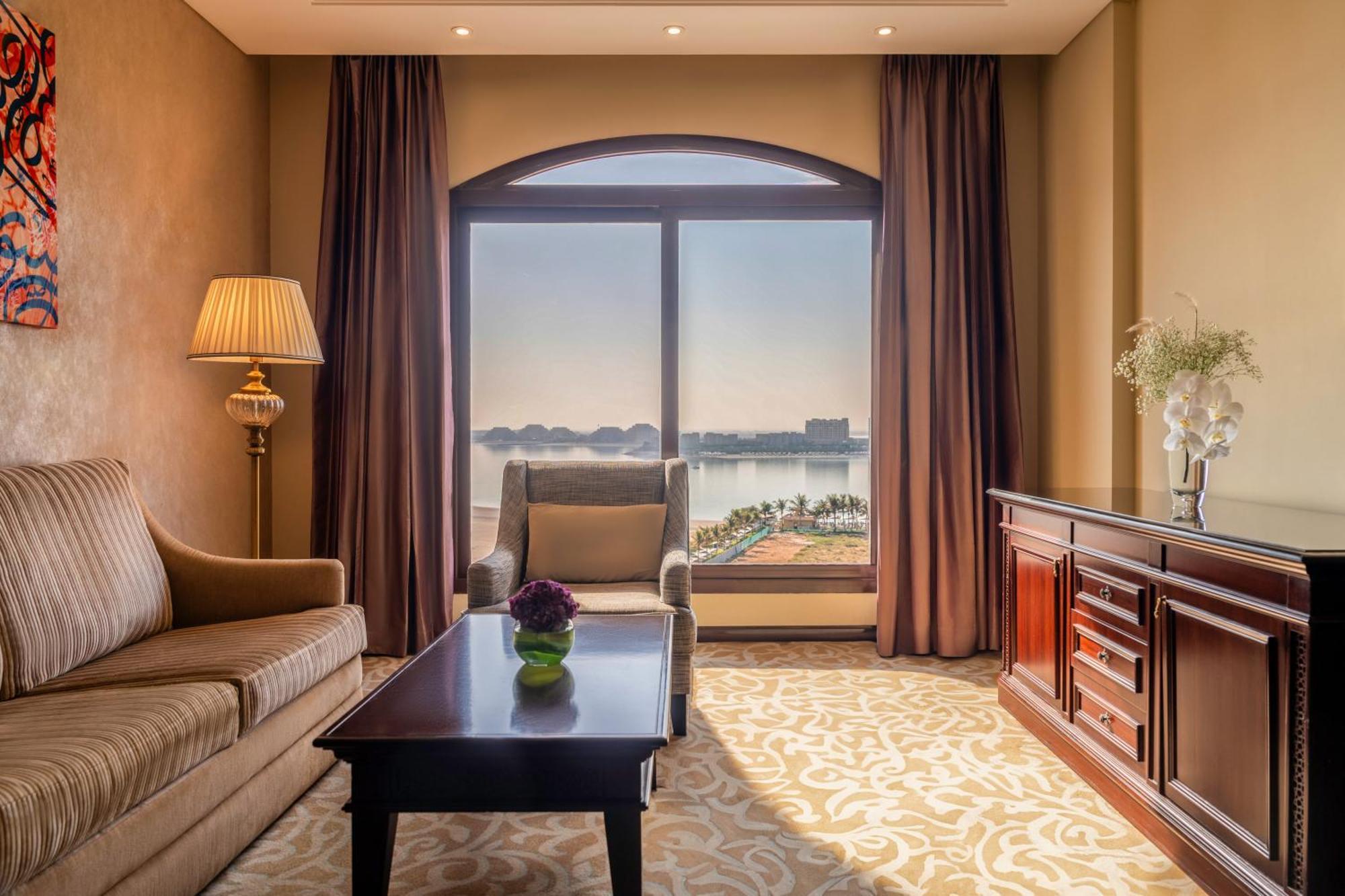 Pullman Resort Al Marjan Island Ras al-Khaimah Exterior photo The photo depicts a well-appointed hotel room or lounge area. It features a cozy seating arrangement with a striped sofa and an armchair, both positioned around a small wooden table. A vase with flowers sits on the table. There is a side lamp providi