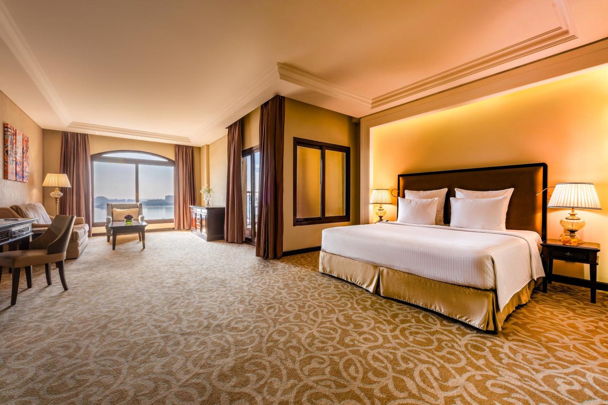 Pullman Resort Al Marjan Island Ras al-Khaimah Exterior photo The photo depicts a spacious and elegantly designed hotel room. It features a large bed with white linens and plush pillows. To the side, there is a comfortable seating area with a sofa and chairs, along with a small table. The room has large windows