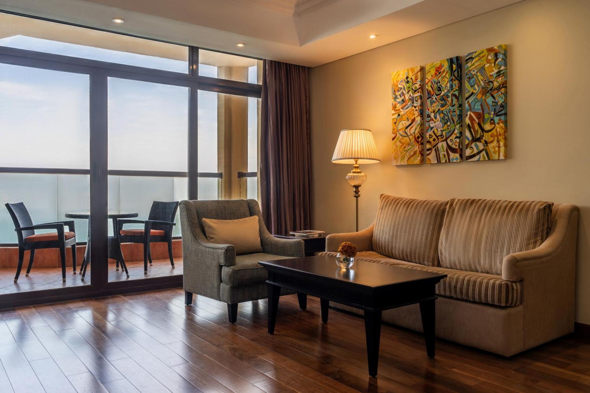Pullman Resort Al Marjan Island Ras al-Khaimah Exterior photo The photo shows a cozy living room area featuring a light-colored sofa with vertical stripes and a grey armchair. There is a dark wood coffee table in front of them. A lamp stands beside the sofa, providing additional lighting. On the wall, there is 