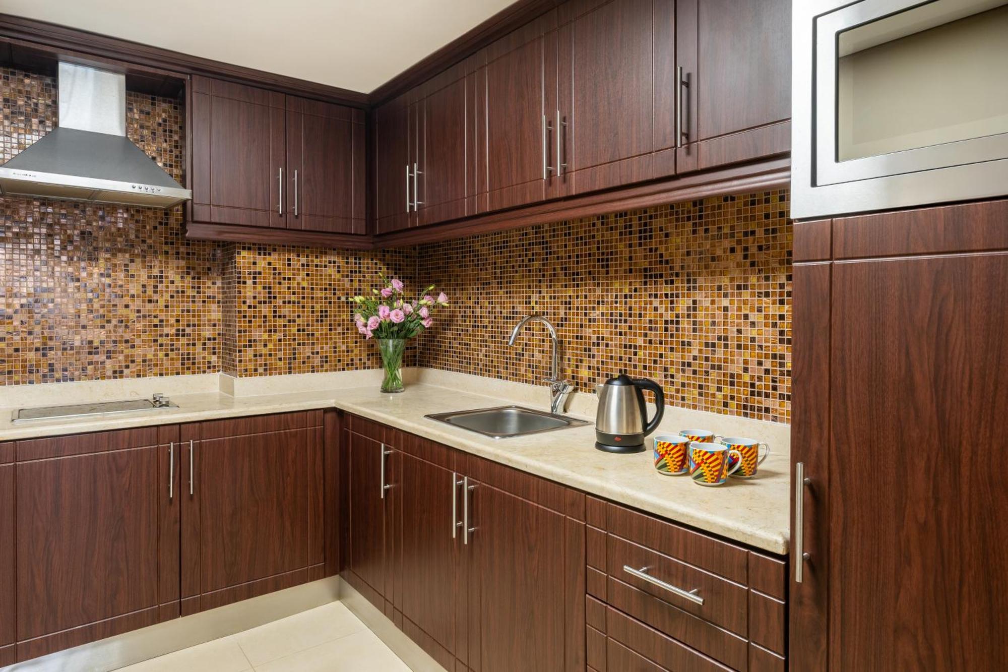 Pullman Resort Al Marjan Island Ras al-Khaimah Exterior photo The photo shows a modern kitchen with dark wooden cabinets and a light-colored countertop. The backsplash features a mosaic pattern of small tiles in various shades, adding visual interest. There is a stainless steel range hood above the stove area. 