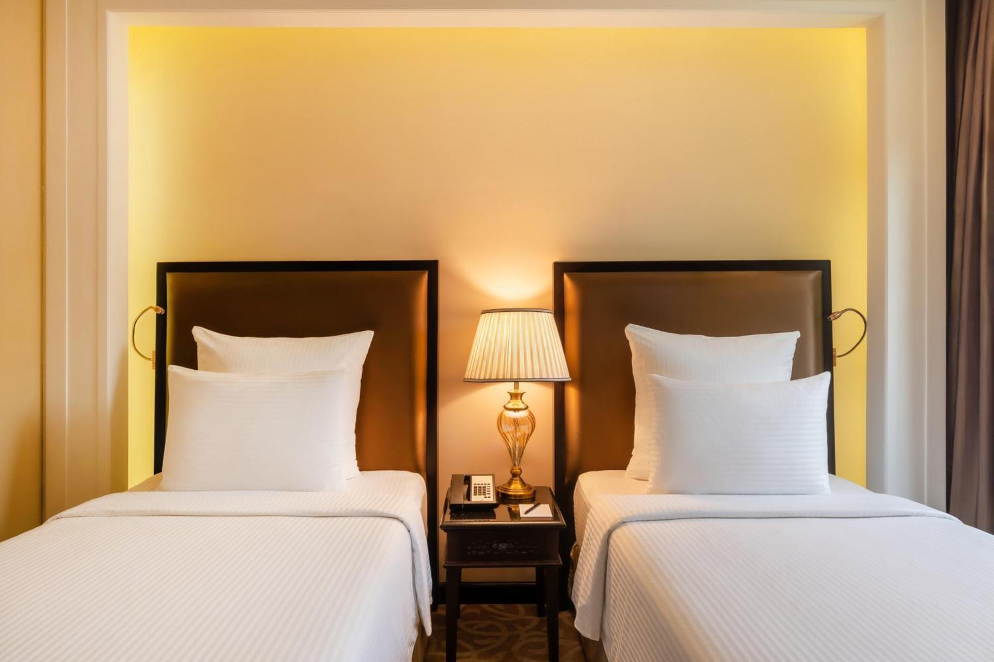 Pullman Resort Al Marjan Island Ras al-Khaimah Exterior photo The photo shows a well-designed bedroom with two twin beds positioned side by side. Each bed is dressed in white linens and has multiple white pillows. Between the beds, there is a bedside table featuring a lamp with a beige shade that emits a warm g