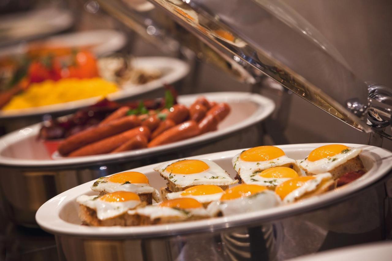 Pullman Resort Al Marjan Island Ras al-Khaimah Exterior photo The photo shows a buffet setup featuring a variety of foods. In the foreground, there are several plates with eggs cooked sunny side up, garnished with herbs. In the background, there are other dishes, including sausages and colorful items like veget